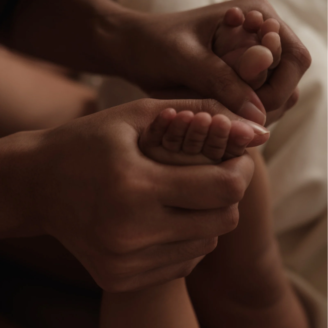 Mutter hält Füße von Baby für Babymassage sanft fest 
